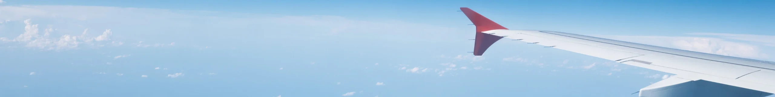 Aircraft wing over cloud layer against a clear blue sky, view from cabin window
