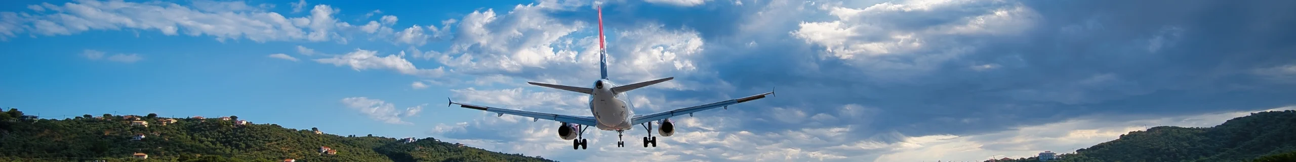 Aircraft on final approach landing over green hills, wide panoramic sky